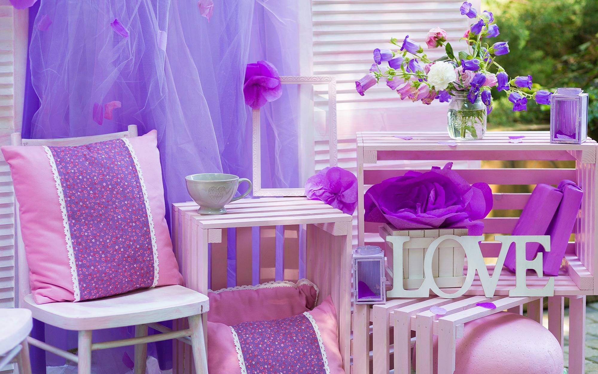 patio setting with wooden chair and crates, pink and purple pillows, flowers, tulle and other outdoor decor